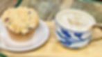 A warm coffee with white foam and spices on top in a white and blue floral cup, next to a blueberry