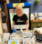 An older smiling woman with white hair wearing a black shirt behind the register.