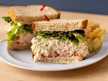 halved chicken salad sandwich with tomato and lettuce and a side of potato chips
