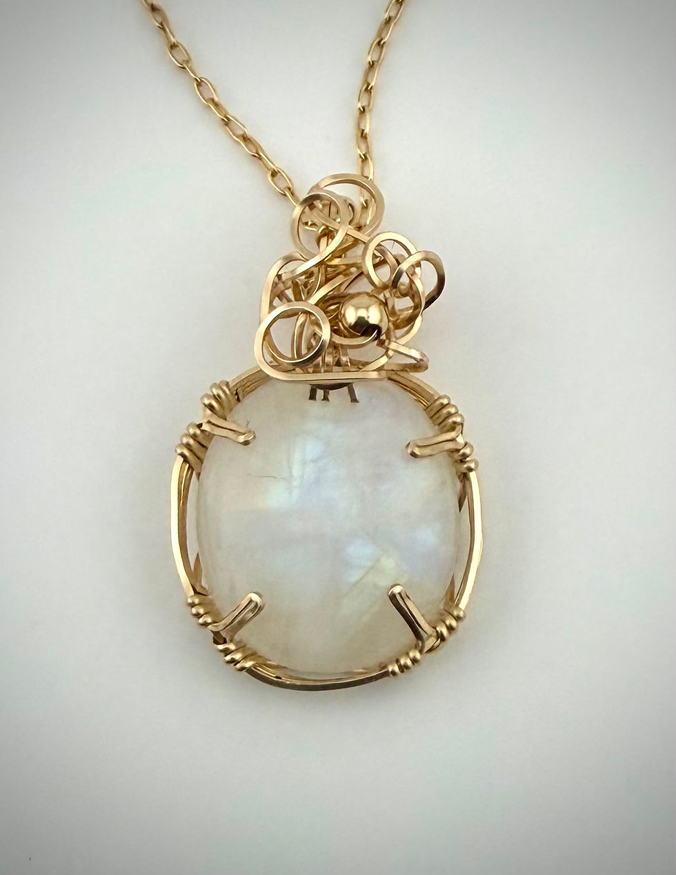 Front view of Moonstone Beauty pendant showing opalescent moonstone and gold wire wrap with delicate swirls.