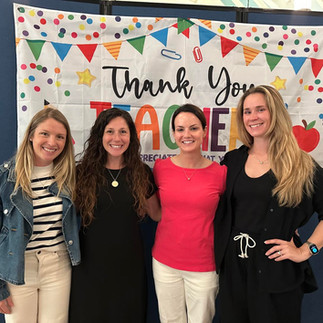four smiling women posing in front of a colorful "thank you teachers" banner