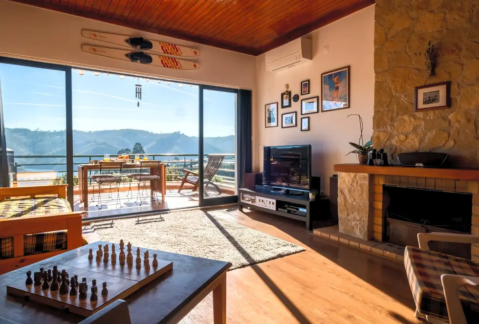 Blue Lake House’s sunny living room, rustic fireplace, and balcony with stunning views of Lago Azul and Castelo de Bode Lake.