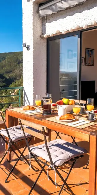 Blue Lake House’s sunny balcony, large outdoor table with breakfast, sun lounger, and bright living room.