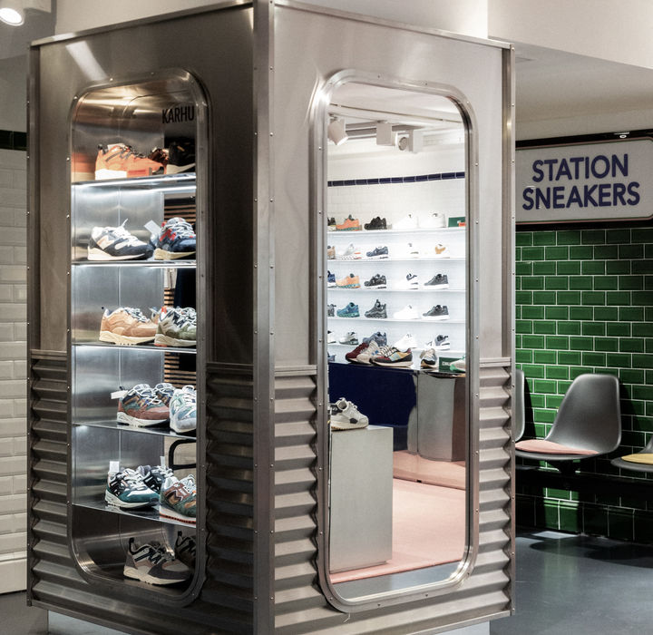 Intérieur d'une boutique de sneakers au design contemporain et épuré. L’espace est organisé autour d’un tapis rose qui contraste avec les matériaux métalliques des présentoirs. Les sneakers sont disposées avec soin sur des étagères rétroéclairées en carrelage blanc brillant, donnant un effet flottant. Des chaises design aux assises colorées offrent un espace d’essayage élégant. L’ambiance mêle influences rétro et minimalisme moderne, avec une palette de couleurs douces et des détails sophistiqués.