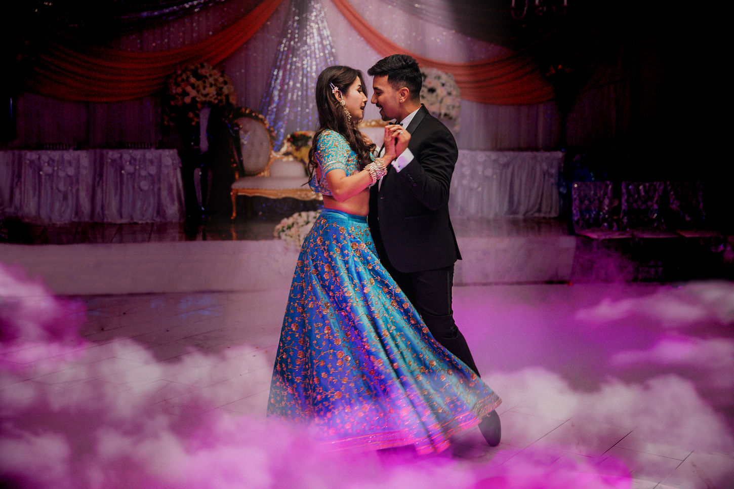 Photo of a couple dancing in a grand ballroom filled with smoke, creating a magical and romantic atmosphere