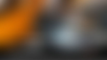 Tattooed arm with black gloves prepares a piercing needle. Person in orange in the background. Text: "First piercing as an adult..."