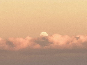 Moon rising above pink clouds at dusk over a hazy valley town