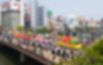 The colourful parade going across the bridge with crowds of people on both sides.