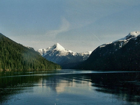 Calm Alaskan fjord with forested mountains and snowcapped peaks reflected in still water; ©MDHarding in bottom right.