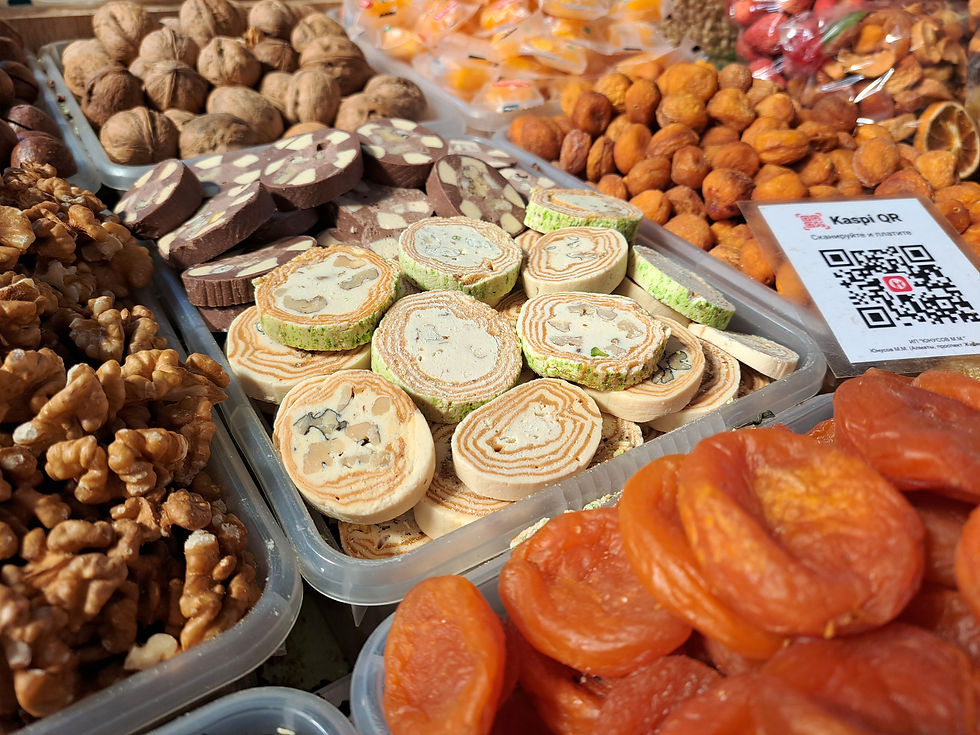 Assorted nuts and dried fruit at a market stall, with sliced nut confections and a Kaspi QR sign.