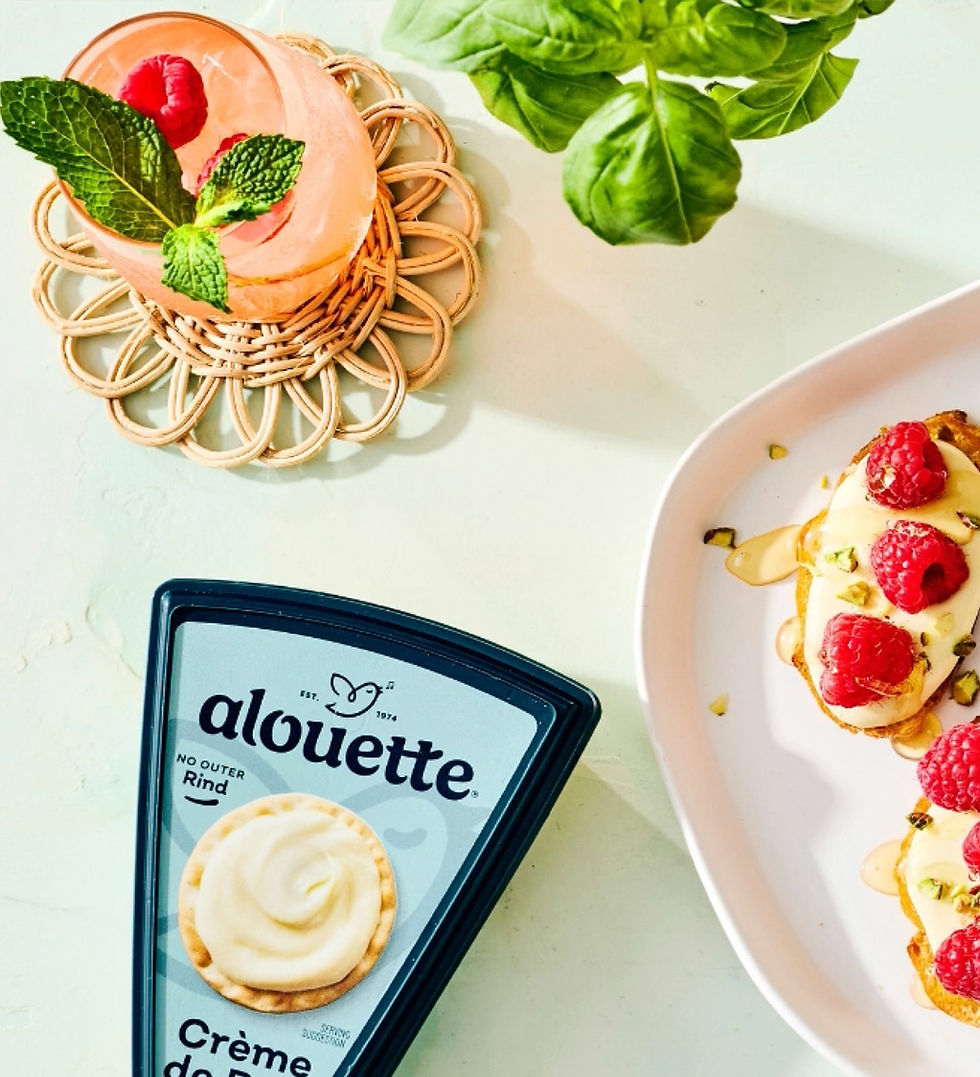 Top-down view of a platter of crostini topped with alouette cheese, raspberries and honey, with a pack of alouette Crème de Brie beside it.