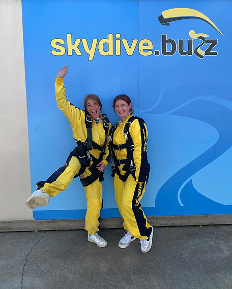 Two staff from the northam care trust after their charity sky dive infront of the Skydive.buzz logo.