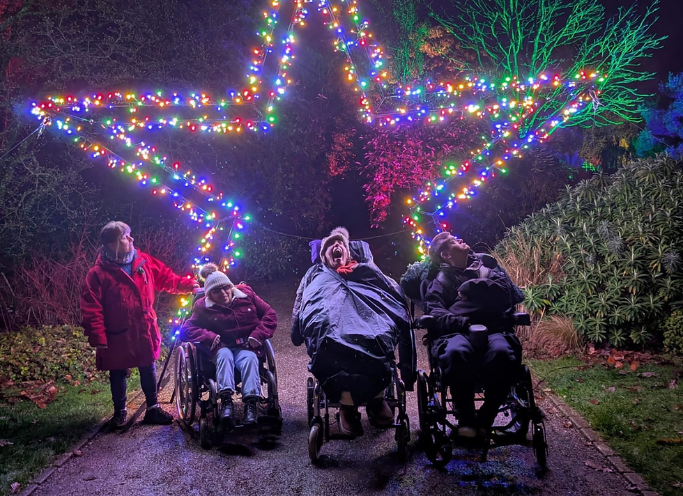 A picture of 4 people we support at Rosemoor Glow in front of a star lit up with multicoloured lights