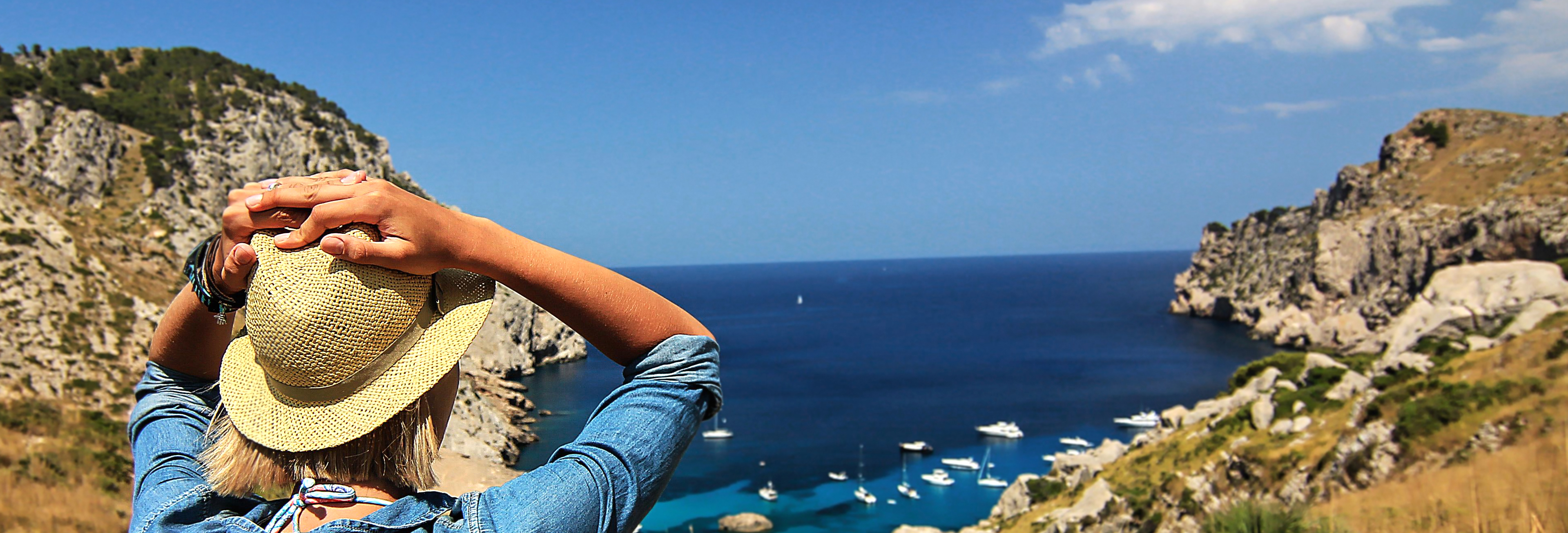 A woman looking at the sea's horizon with boats and cliffs in sight.