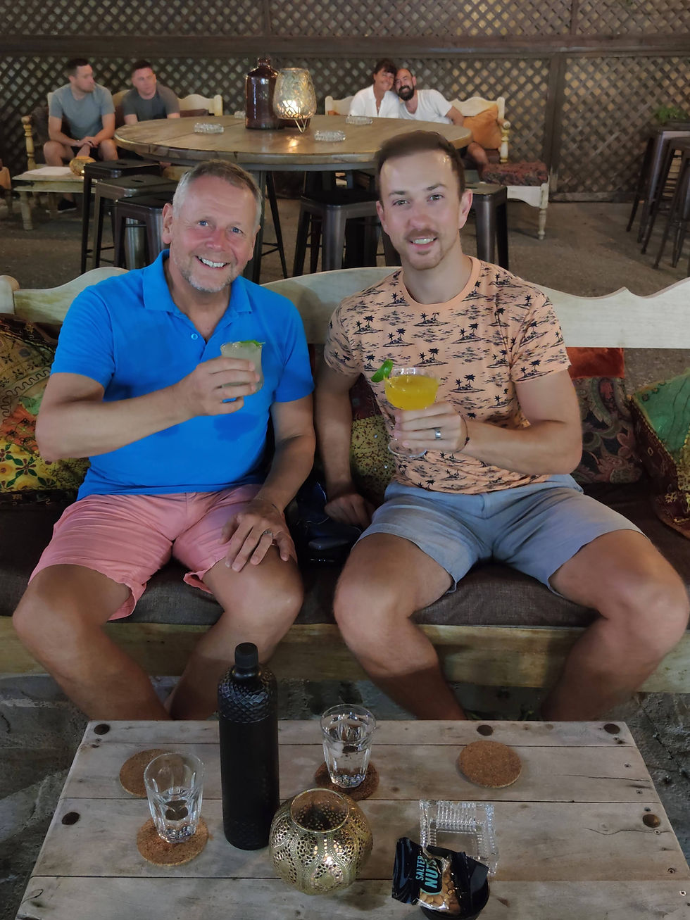 Age gap gay men with cocktails sitting on bench