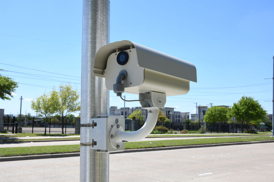 A speed camera mounted on a pole by the roadside, capturing the speed of passing vehicles