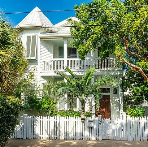 sunny image of the front of a white two-story house with a white picket fence listed in The Meadows area listed by Key West real estate group, ShineGroup