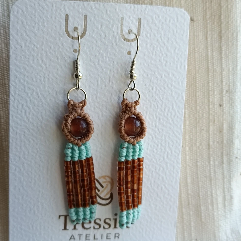 Boucles d'oreilles pendantes artisanales en macramé marron et turquoise avec une perle ronde, montées sur une cartonnette
