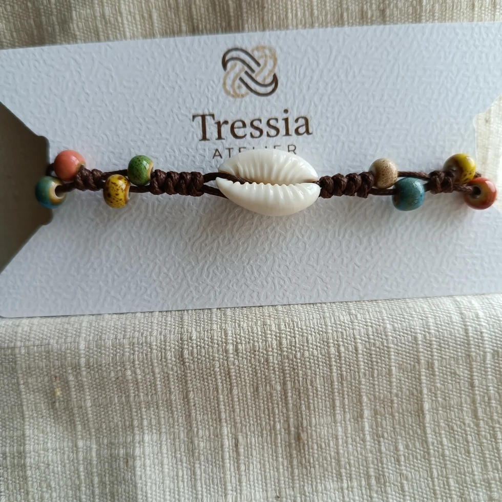 Bracelet en macramé avec coquillage cauri et perles en porcelaine multicolores présenté sur carte Tressia Atelier