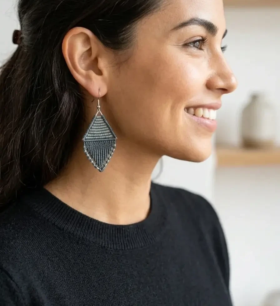 Portrait de profil d'une femme souriante portant les boucles d'oreilles Vesper gris orage sur un pull noir - Tressia Atelier