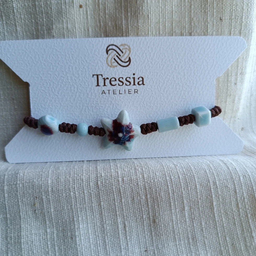 Bracelet en macramé fait main avec perle étoile en porcelaine bleue présenté sur carte Tressia Atelier sur fond textile lin