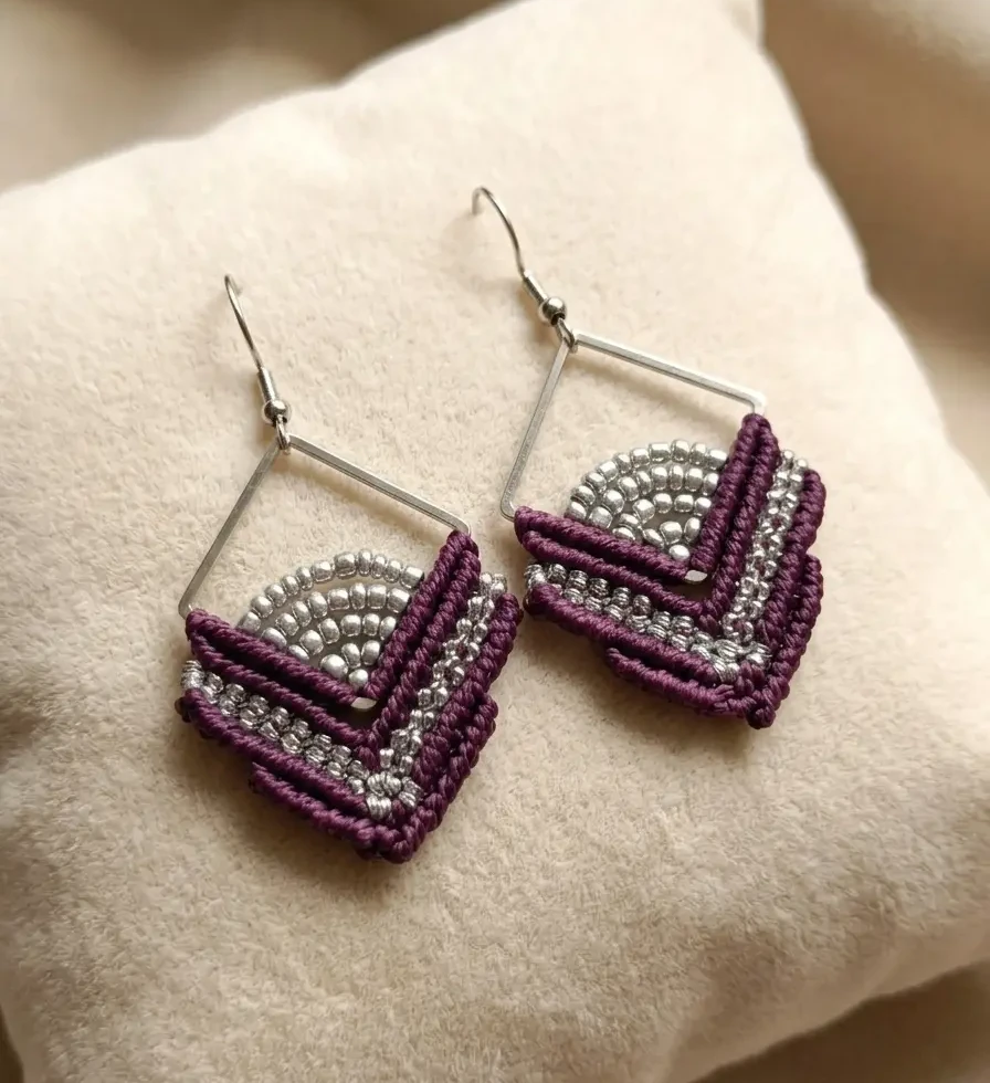 Boucles d'oreilles ISO en micro-macramé violet et perles argentées, présentées sur un coussin beige - Tressia Atelier