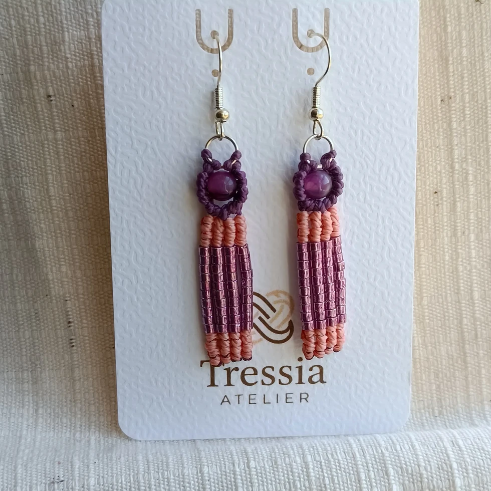 Gros plan de boucles d'oreilles faites main en macramé violet, perles de rocaille roses et une perle centrale violette