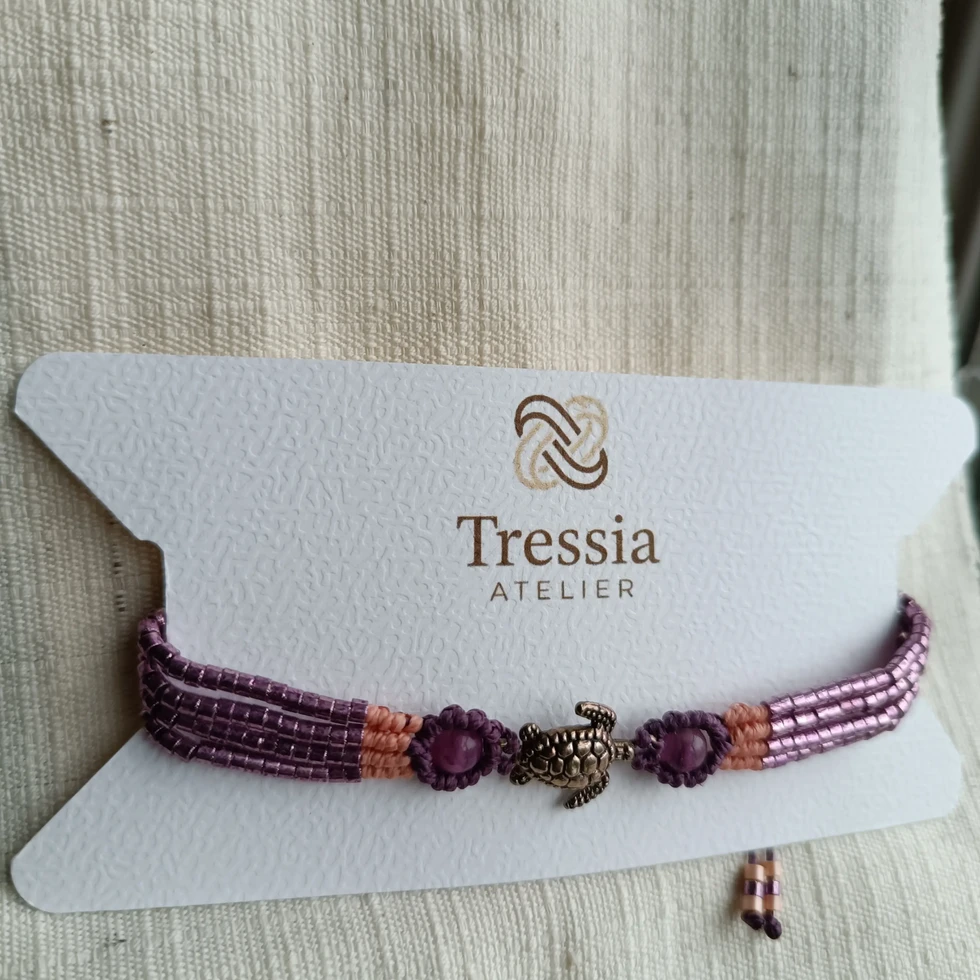 Bracelet Alya fait main violet et rose en perle et micromacramé présenté sur une cartonnette Tressia Atelier