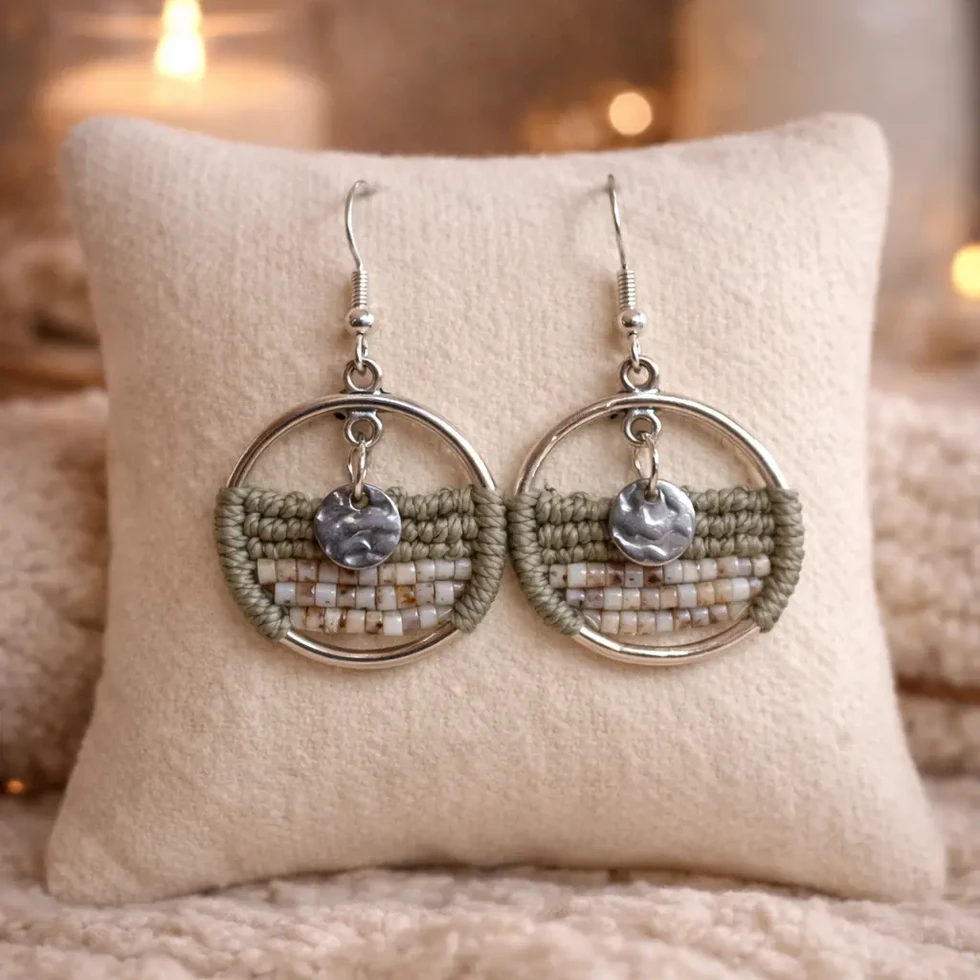 Gros plan des boucles d'oreilles Sélia Sauge montrant le cercle argenté, le tissage en perles vert sauge et crème.
