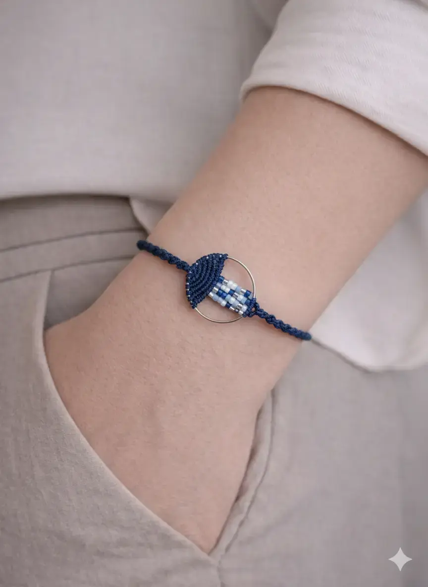 Bracelet macramé bleu avec perles tissées et cercle métallique, porté au poignet.