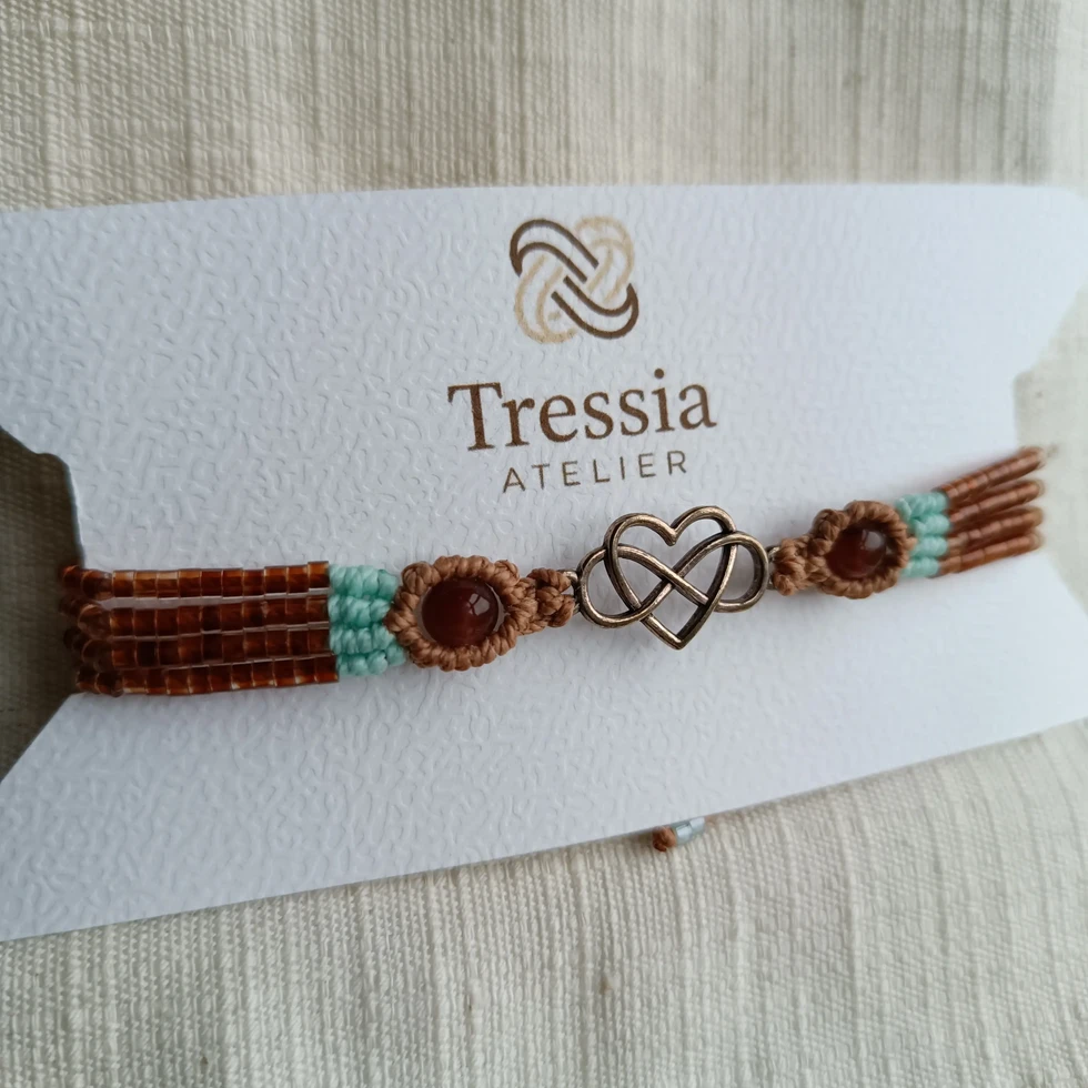 Photo sans IA du bracelet Alya artisanal marron et turquoise en micromacramé présenté sur une cartonnette Tressia Atelier