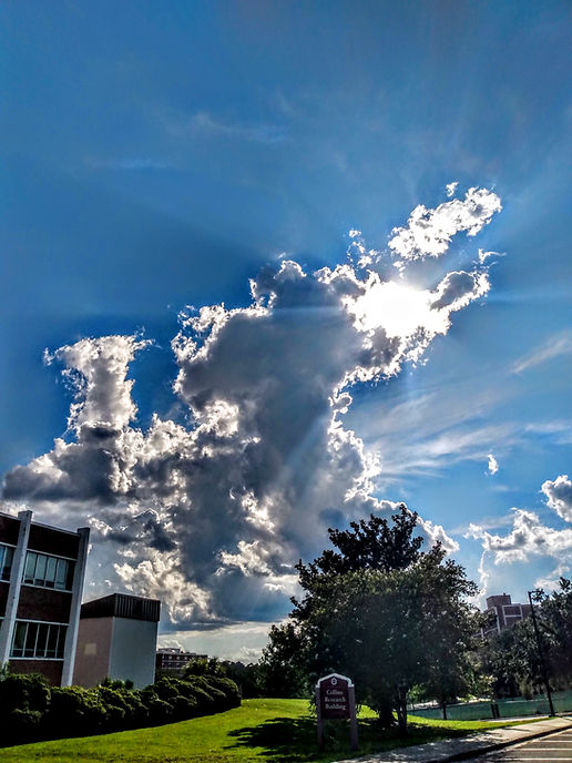 It is an original shot of the sky with the greater light shining through the clouds. In the Background the Florida State University School Department building is seen. There are trees as well. The focus is the light shining through the clouds.