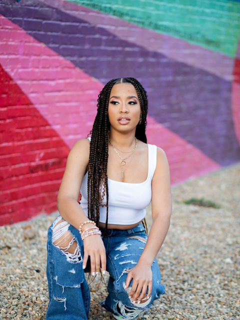 High School senior female kneeling posed in front of colorful mural. 