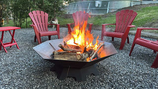 Octagon fire pit painted black on rocks with red chairs in the background.