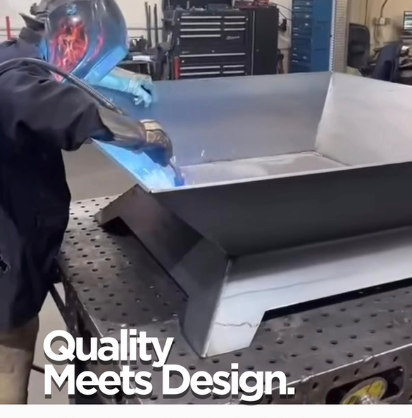 a welder is welding a large fire pit on a fabrication bench