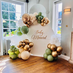 The baby shower personalised backdrop with a balloon garland in gold, white, cream and green colours