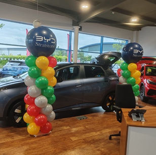 Personalised Balloon tower for a corporate event at the car dealership. The balloon tower is made in red, green, yellow and grey colours with a navy blue top.
