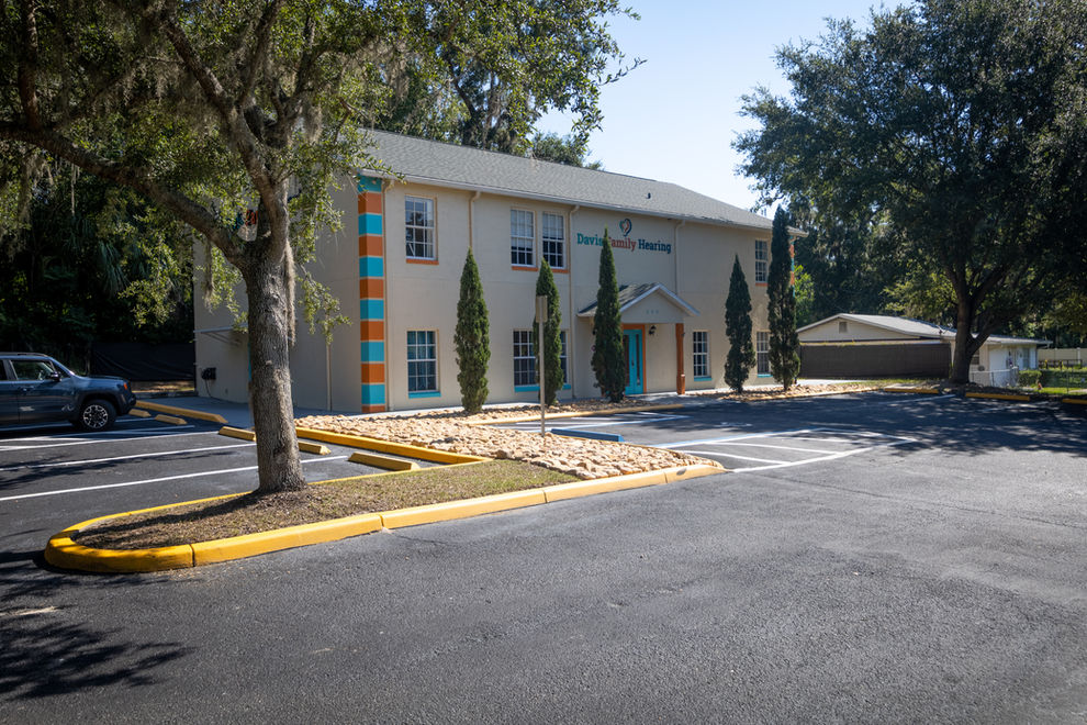 Building with teal door and orange stripes, trees, and parking area