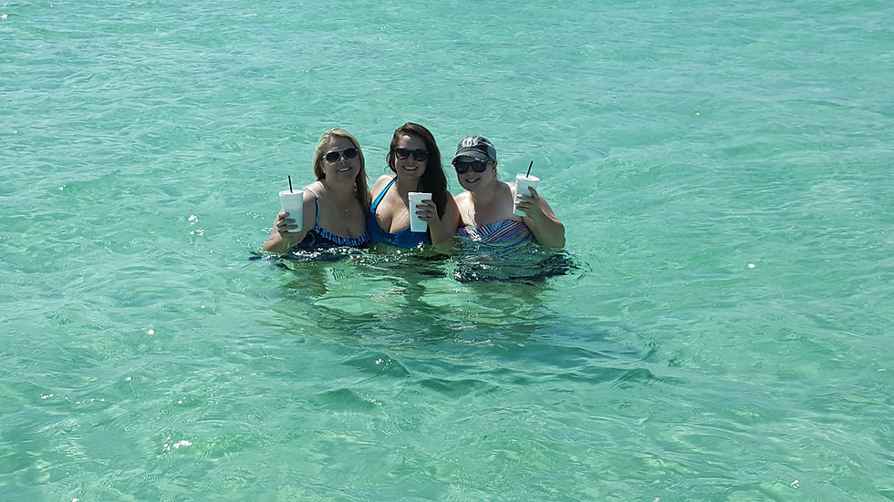 Three women in swimsuits, holding cups, while standing in clear water