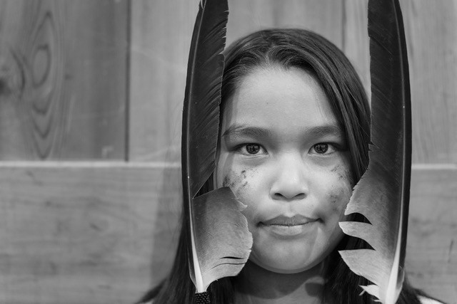 An Indigenous child in Canada peers through two feathers.