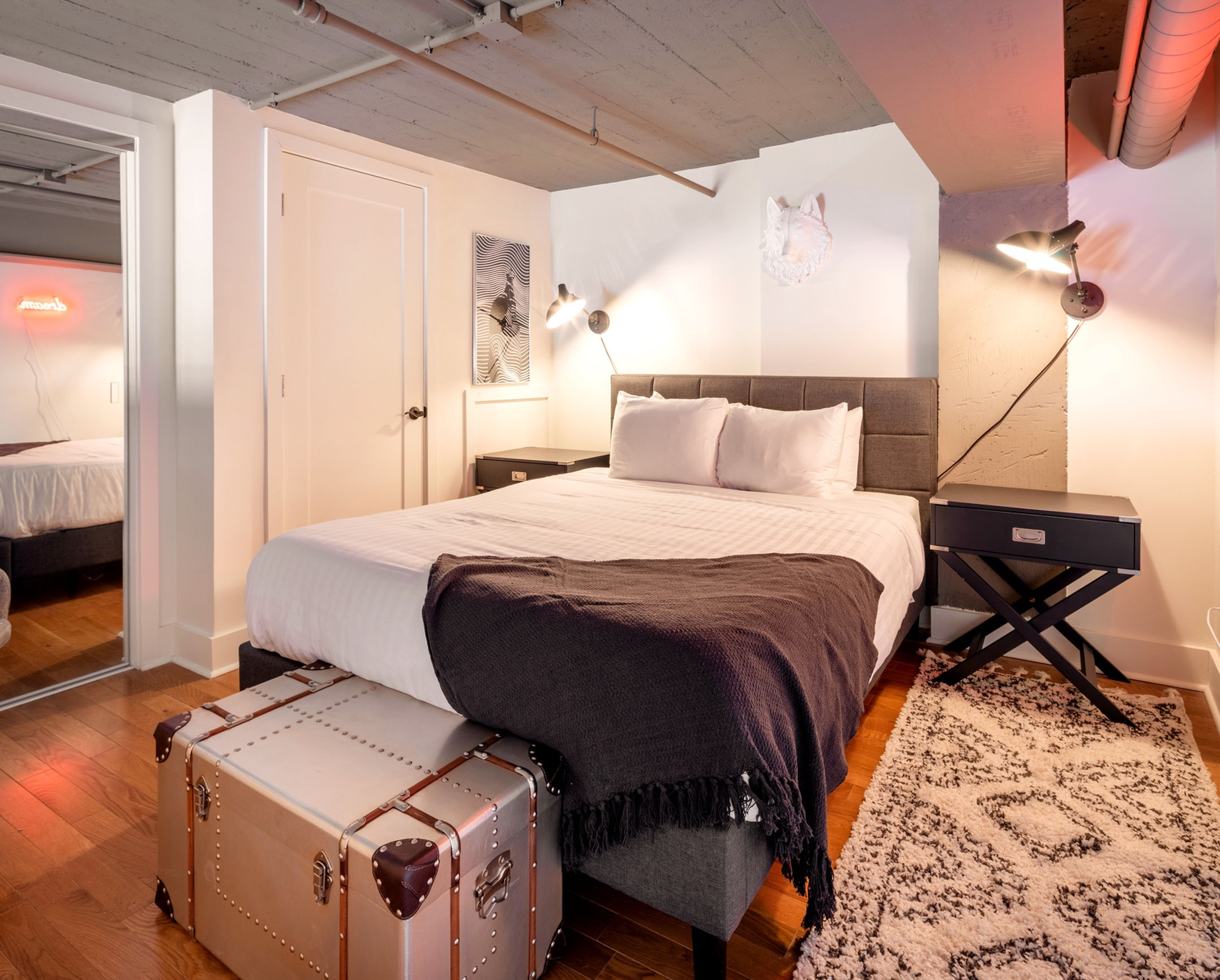 Furnished bedroom with hardwood flooring, a trunk at the end of the bed, and mirrored sliding closet doors