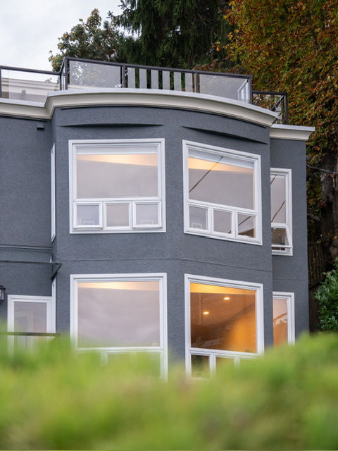 Exterior detail of a gray house with clean lines, large windows, and well-maintained landscaping