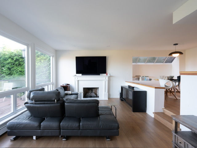 Modern living room with a sleek black leather sectional, large windows, and abundant natural light
