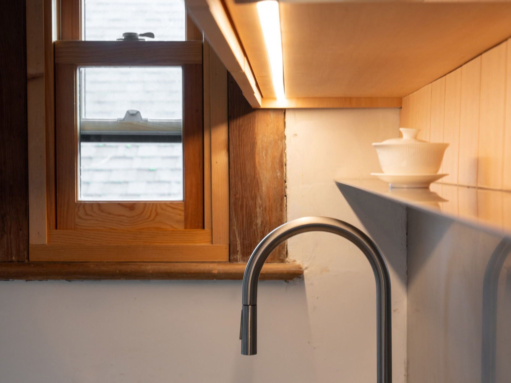 Modern kitchen sink with a sleek faucet, natural wood framing, and soft natural light from a nearby window
