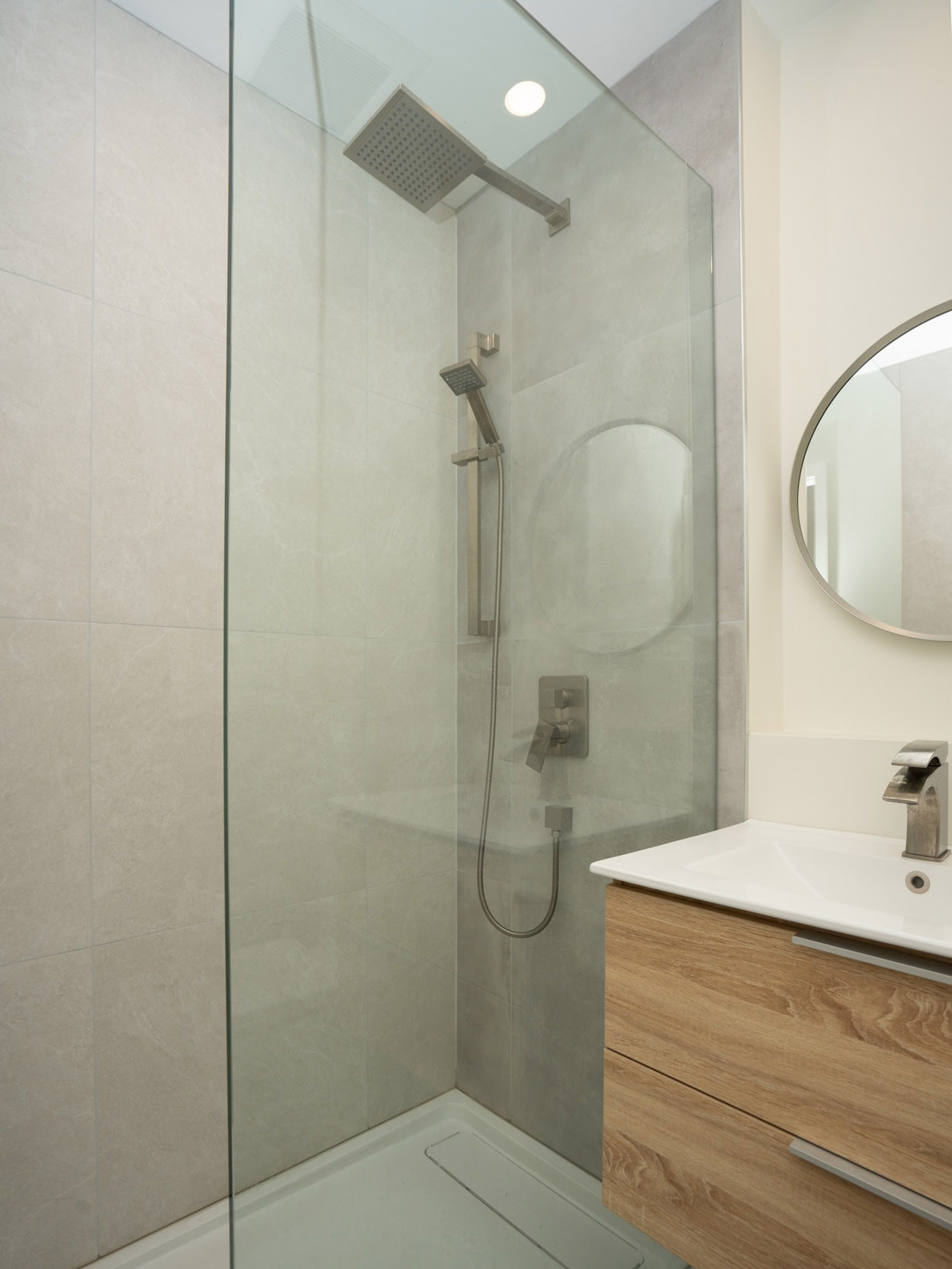 Glass-enclosed shower with a modern rain showerhead, sleek fixtures, and minimalist tiles