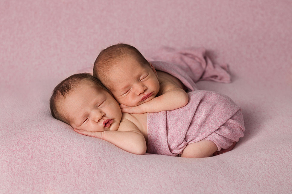 Twin newborn baby girls wrapped in pink