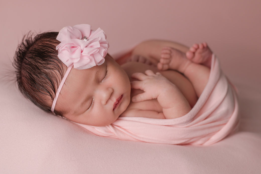 Newborn baby girl wrapped in pink with flower headband
