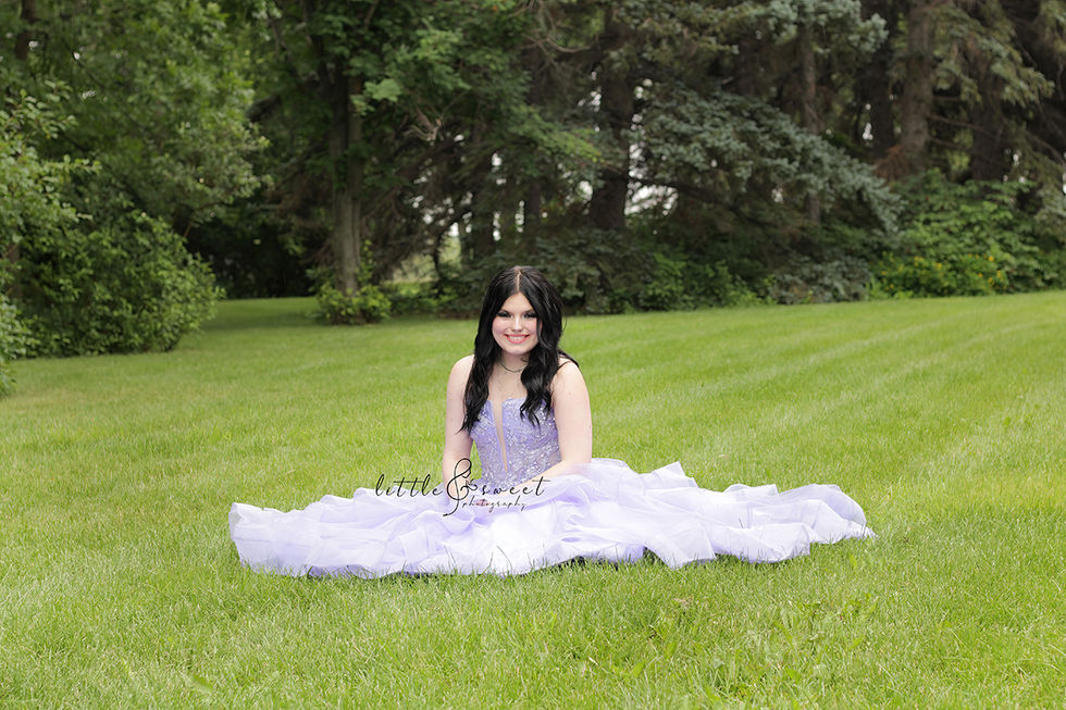 Graduate in lavender gown surrounded by greenery in a lush park
