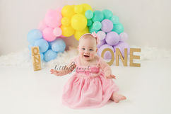 Twin boy and girl first birthday with colored pastel balloon arch and gold one letters for first birthday