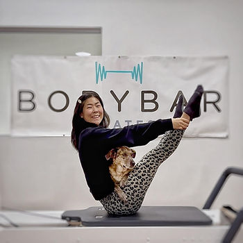 BodyBar Pilates owner/instructor Joyce Ko and her dog Cora hold a teaser pose on a reformer.